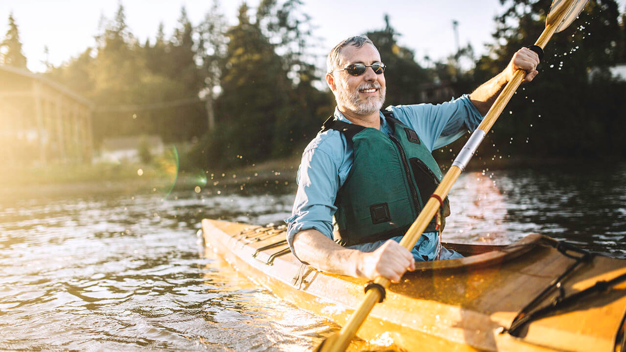 middle aged man paddling in a yellow kayak on a lake
