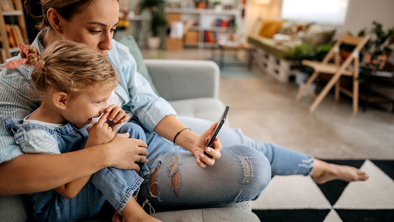 mother holding daughter in arms both smiling looking at phone