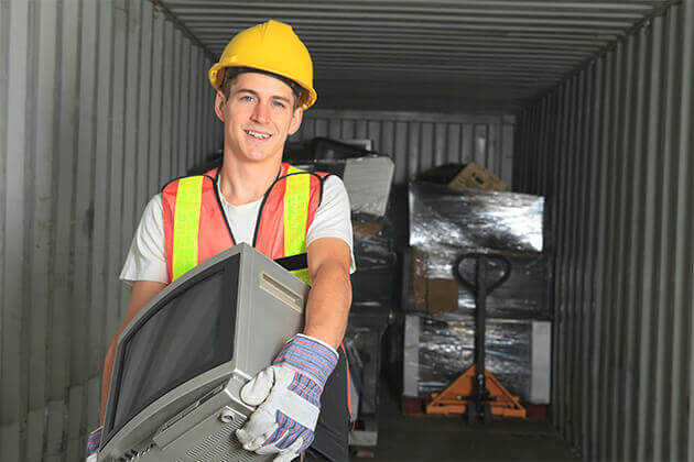 Young man walking out of storage container holding a tv 