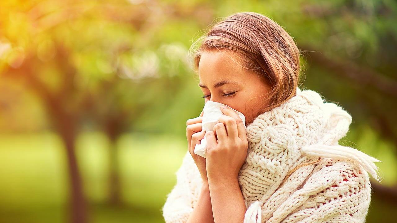 Woman outside wearing a sweater and scarf and blowing her nose