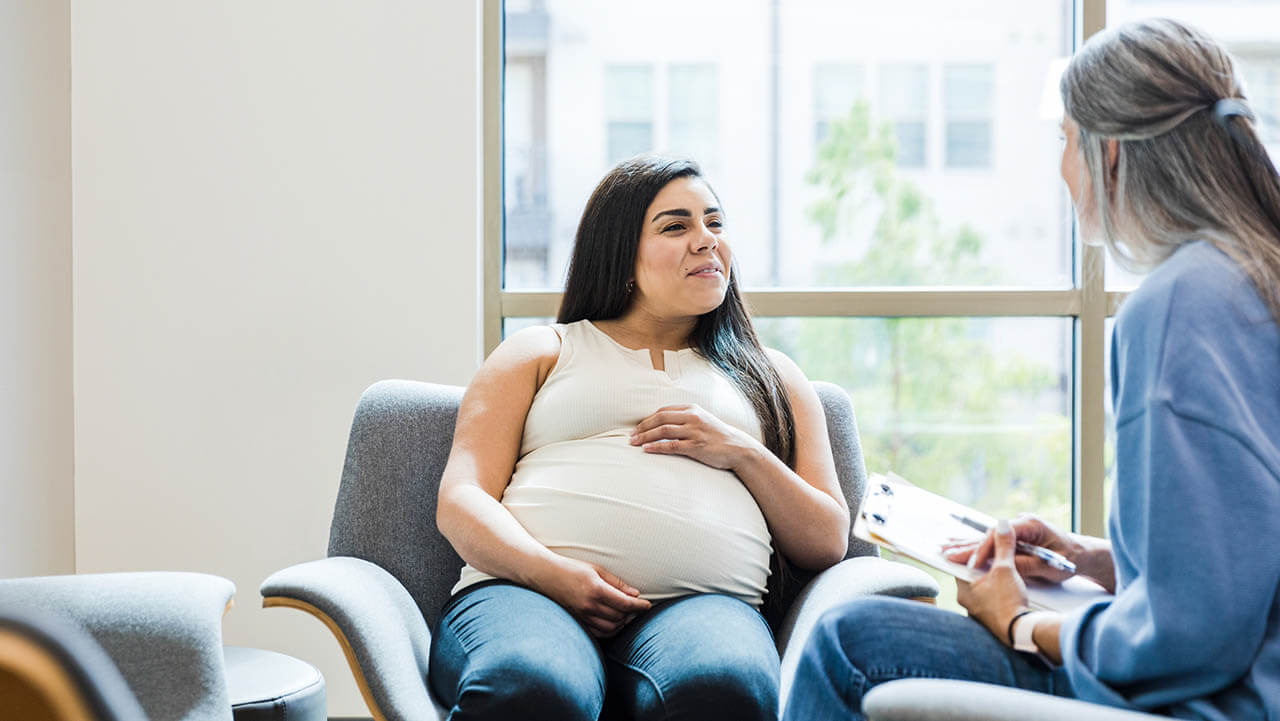 A pregnant women sitting on a chair talking to a midwife