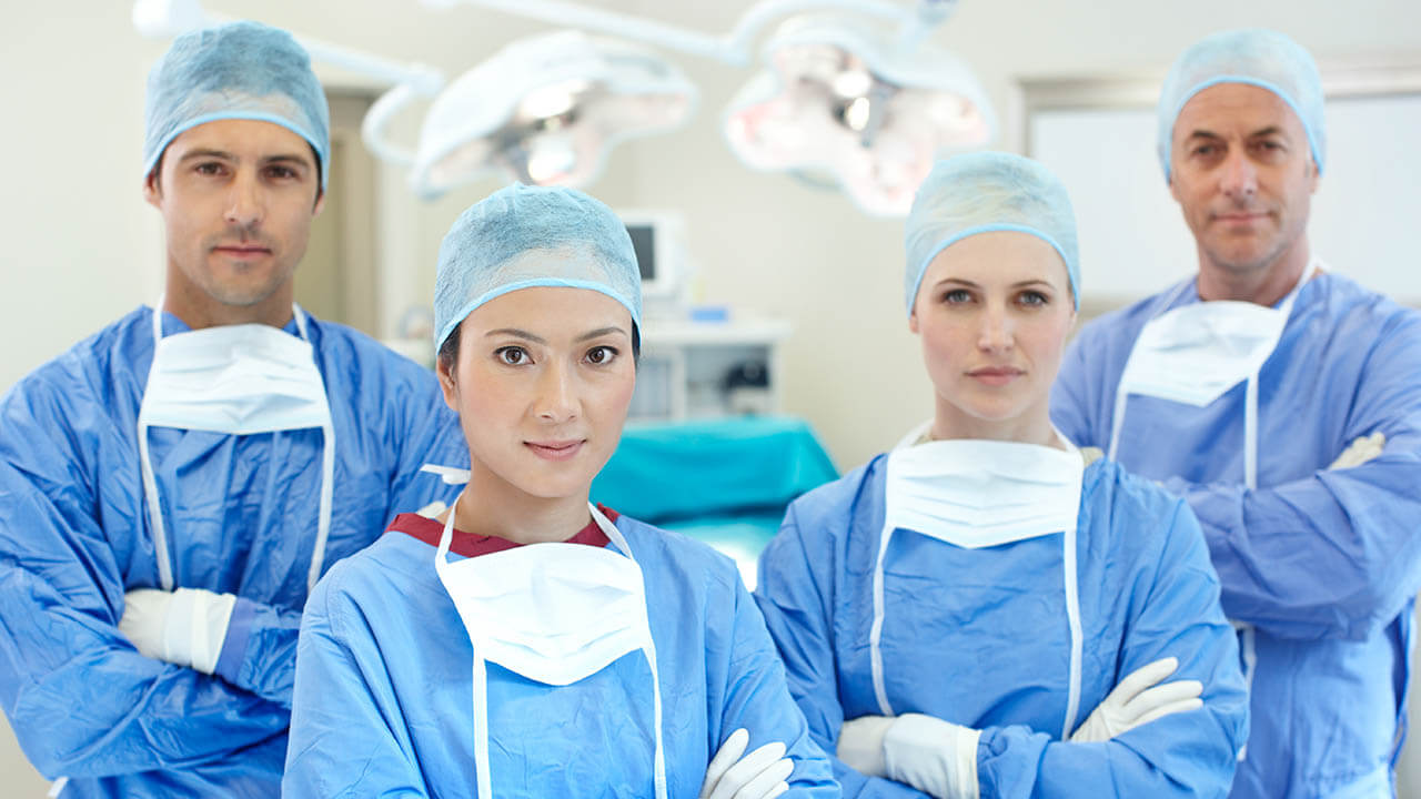 Four surgeons standing next to each other with arms crossed and masks untied