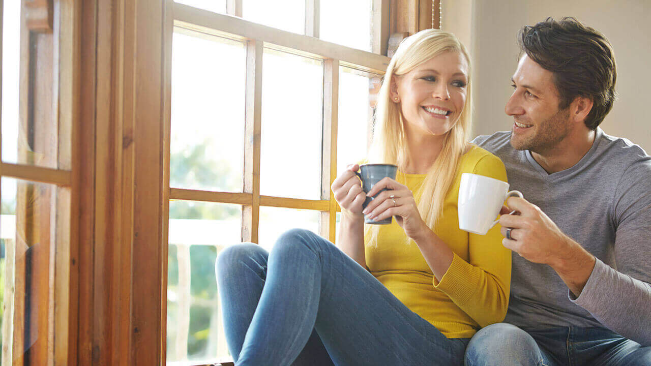 Male and female sitting by window holding coffee mugs