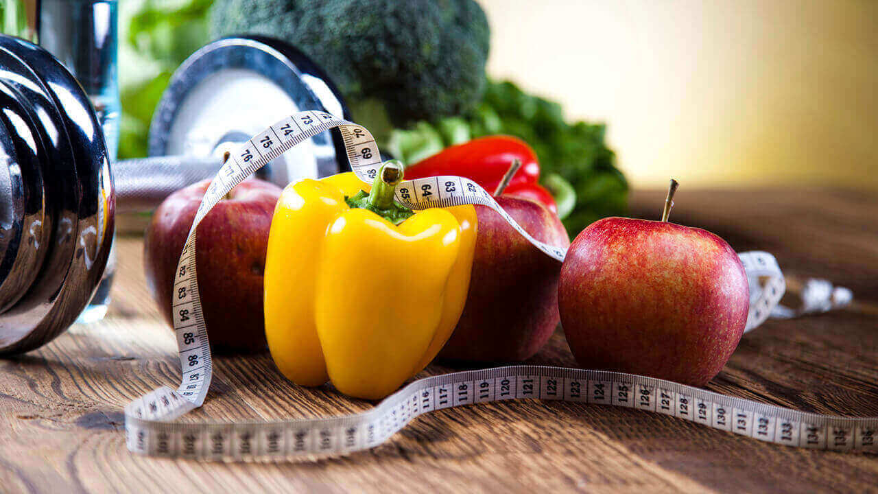 Weight, peppers, an apple, broccoli and a tape measure on a table