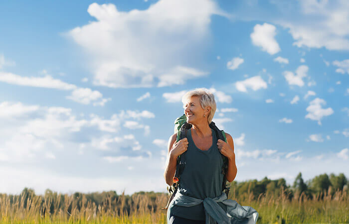 Middle agd woman hiking with a backpack on shoulders through long grass