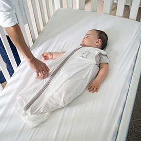 baby swaddled in a sleep sack laying on back in crib