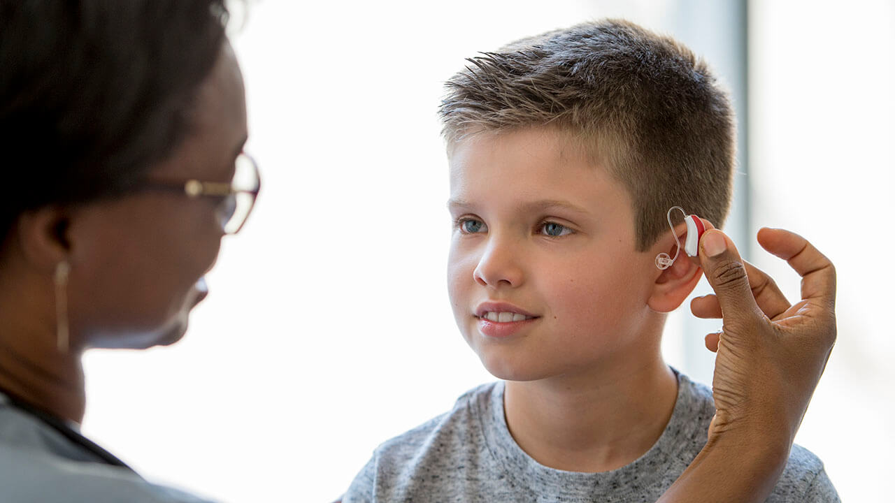 Female audiologist placing hearing aid in young boy's ear
