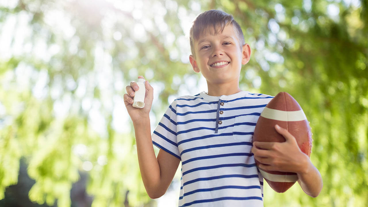 Young boy holding a football and an inhaler smiling