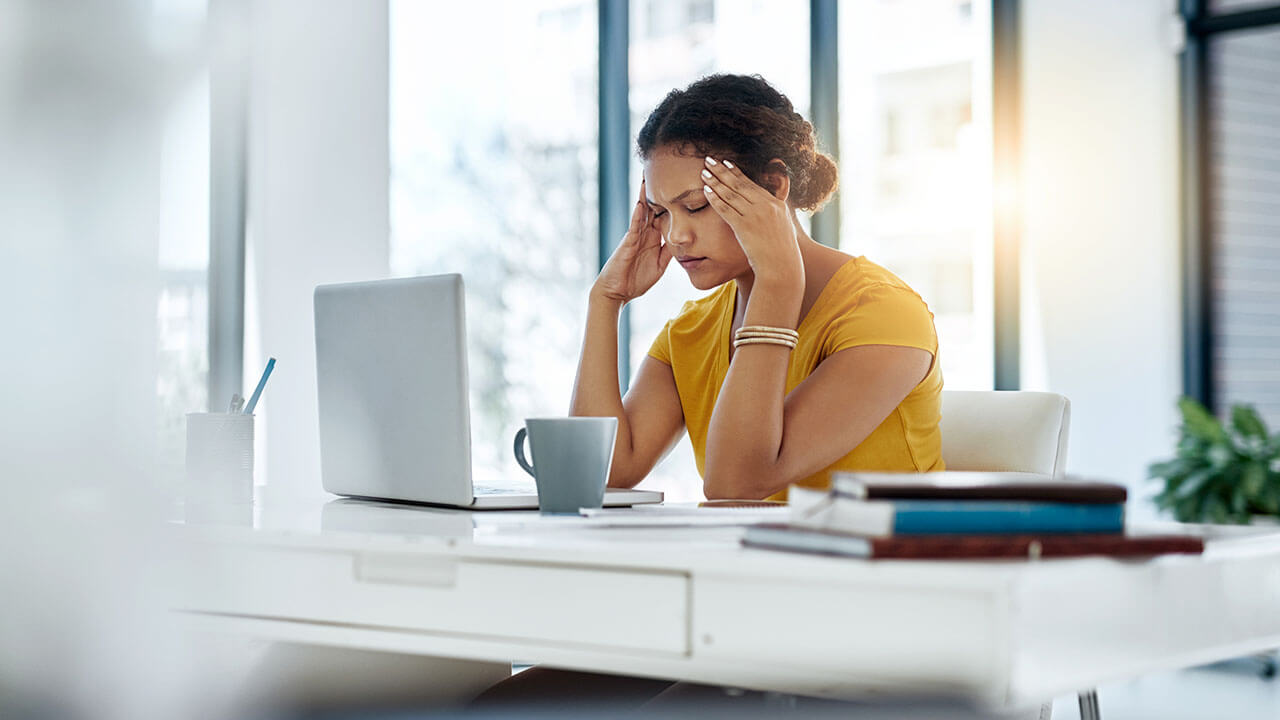 Female woman sitting at desk with computer with closed eyes and pressing hands against her temples