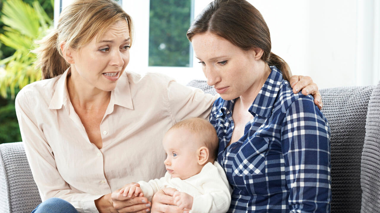 Two women sitting on couch looking at a baby