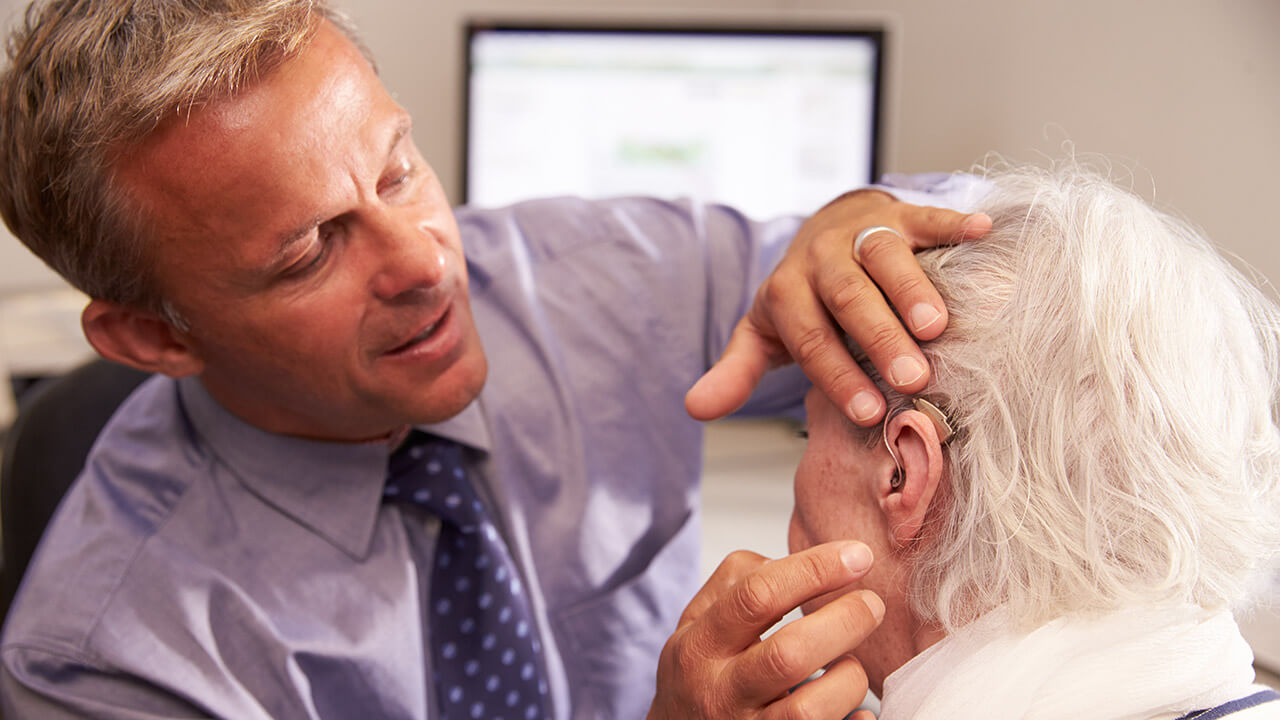 Male audiologist placing a hearing aide in a senior woman's ear