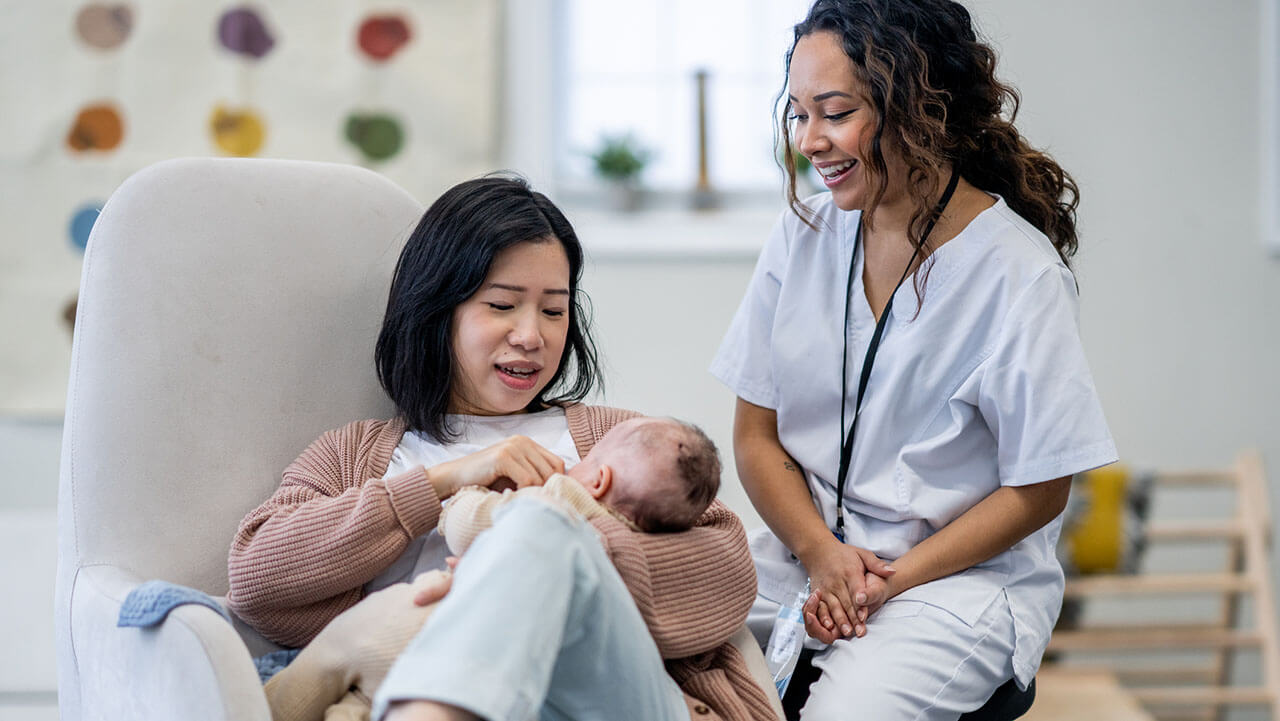 Young mom learning how to breastfeed her newborn baby with a lactation counselor sitting nearby