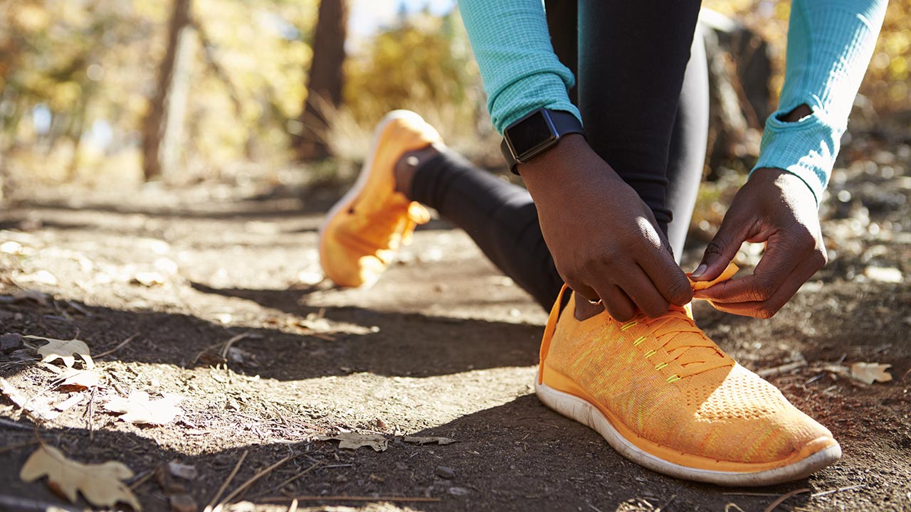 Person tying shoe laces on dirt path