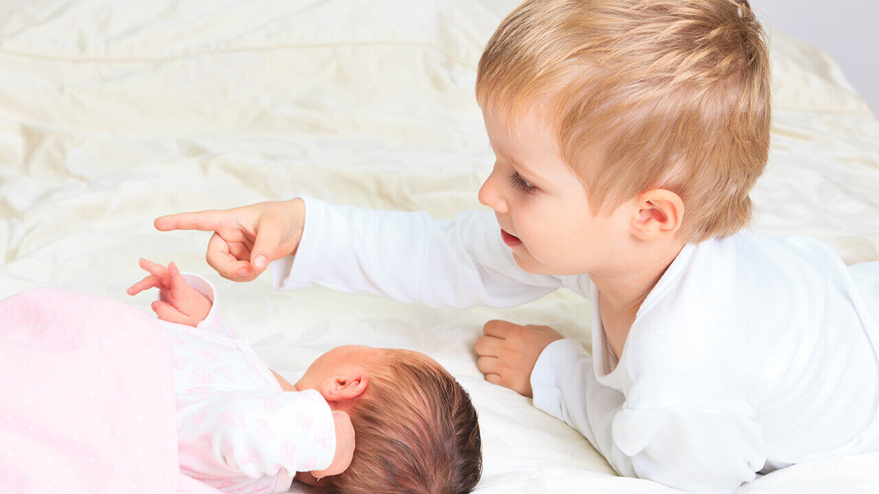 toddler laying on bed with baby