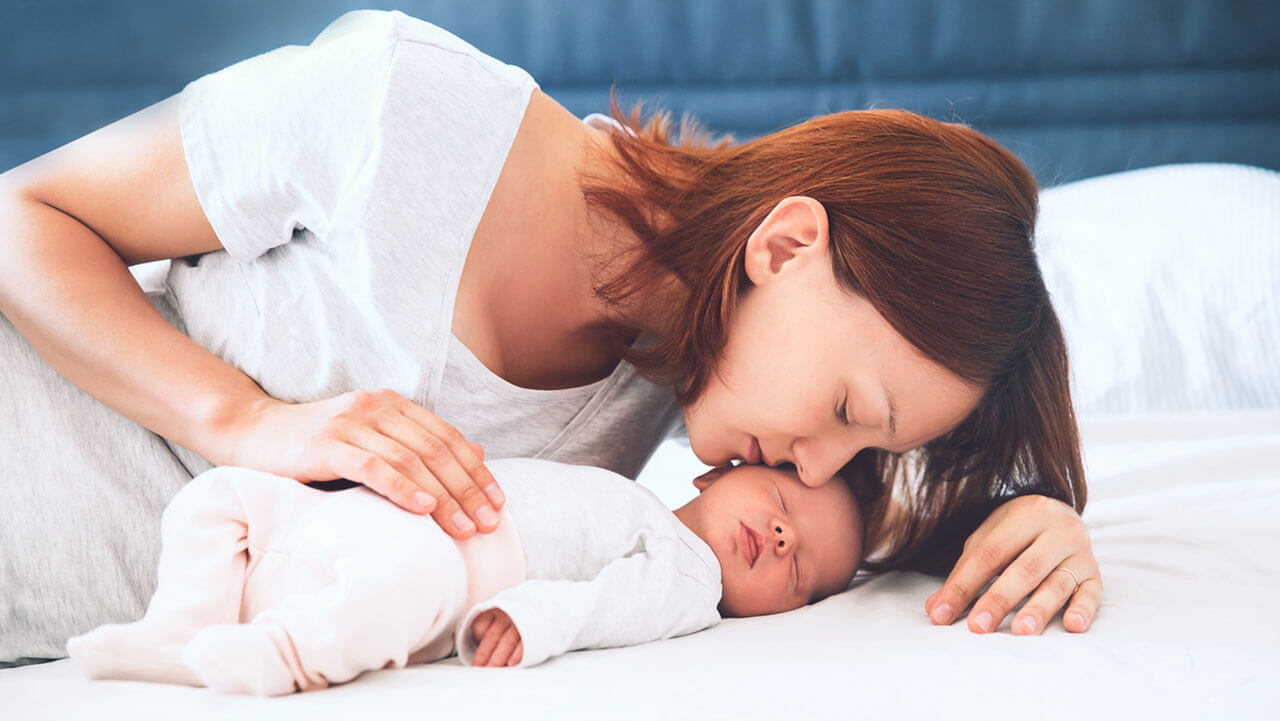 Mother kissing newborn baby on bed