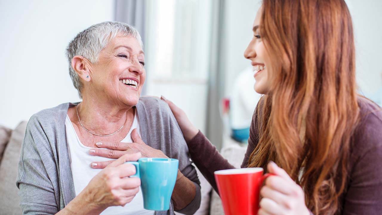 Two women laughing while holding coffee mugs