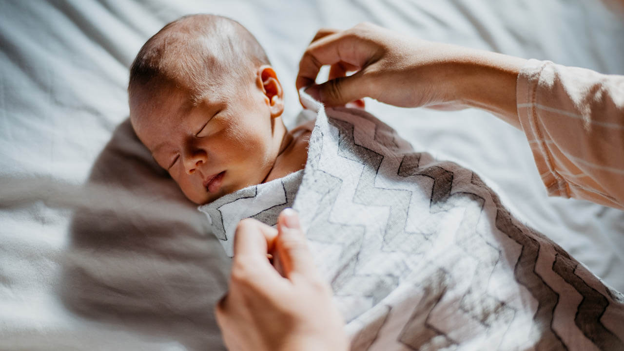 baby swaddled in a sleep sack laying on back in crib