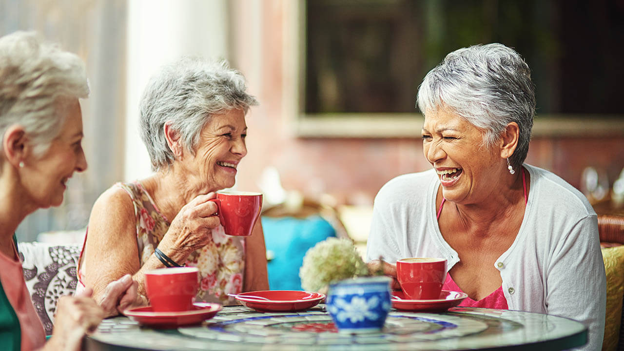 Senior women sitting around a table laughing and holding coffee mugs