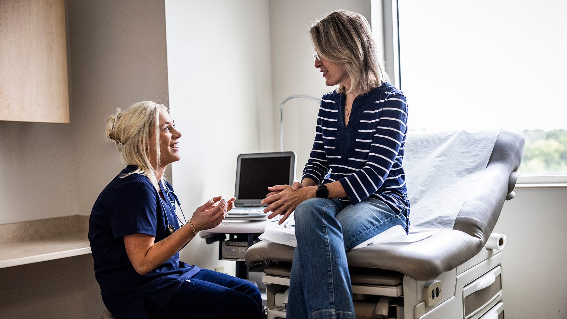 Female doctor in scrubs consulting with senior woman in exam room