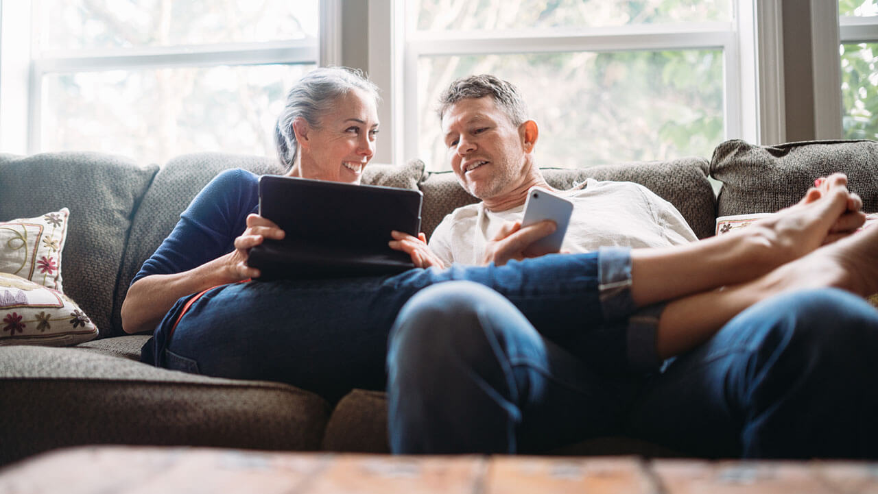 Middle age couple sitting on the couch and looking at an ipad screen