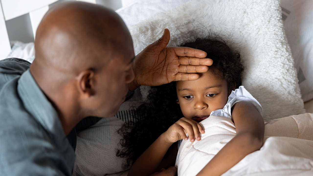 middle aged black father checking forehead temp of young daughter