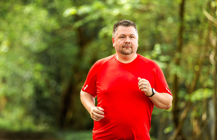 middle aged man jogging on a trail through the woods