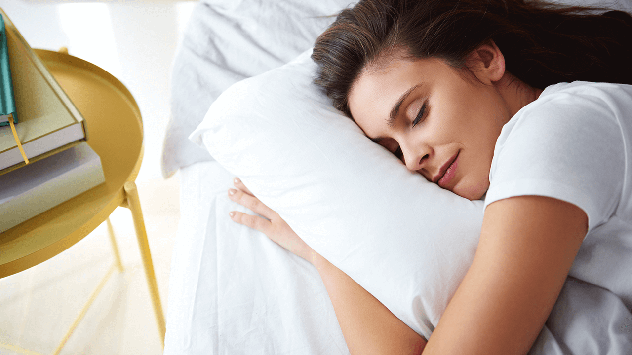 white woman with brown hair sleeping with arm under a pillow
