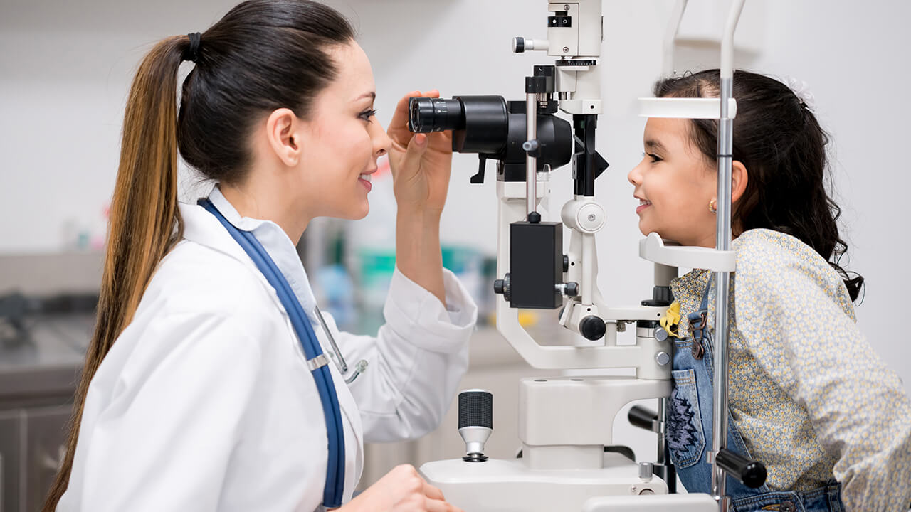 female optician performs eye exam on a young girl using eye exam machine