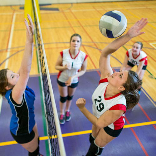 group of teenage girls playing volleyball one is jumping to spike the ball