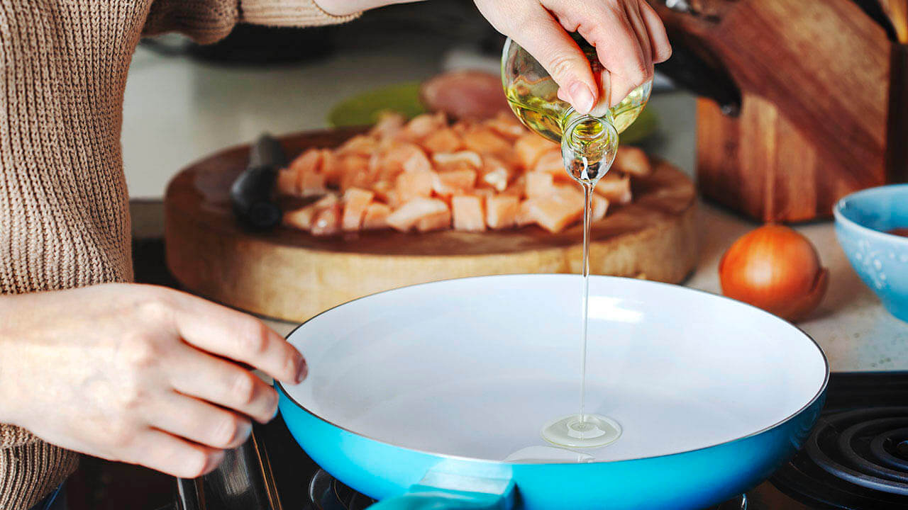 Woman cooking on a stove with a blue frying pan and cooking oil
