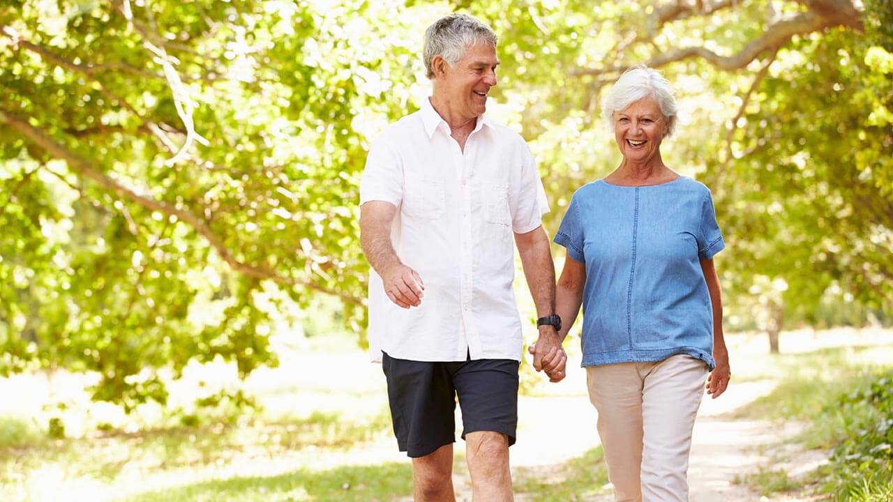 Middle aged man and woman holding hands while walking side by side outside