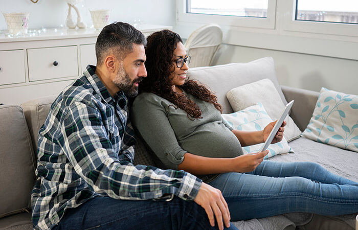 pregnant woman and middle aged man sitting on couch looking at tablet