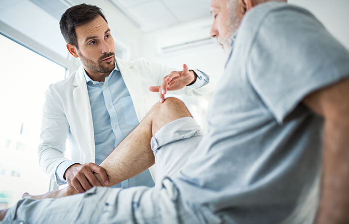 male doctor checking older patients knee for a surgery consult