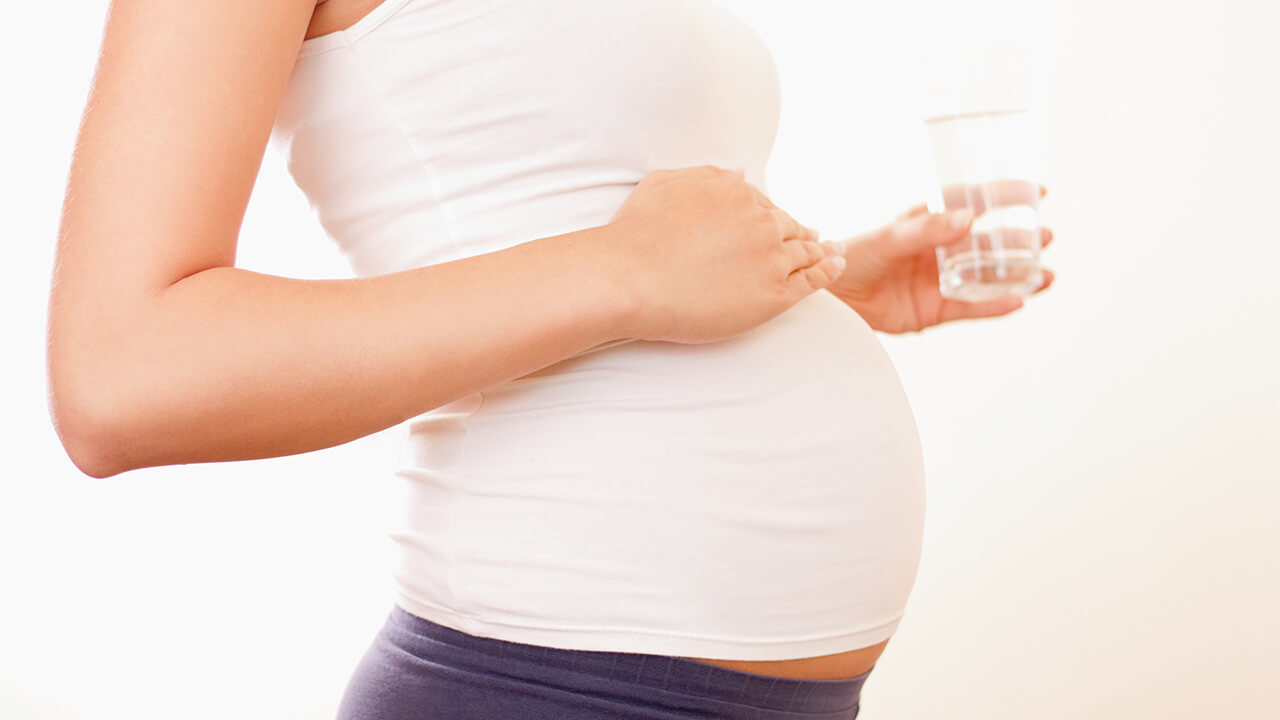 Woman holds glass of water and her belly