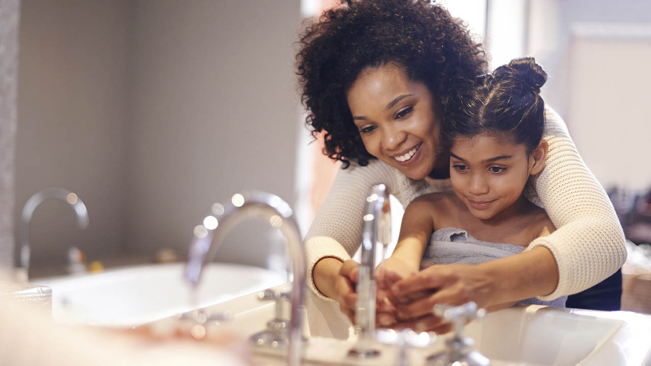 Mother helping her daughter wash her hands at the sink