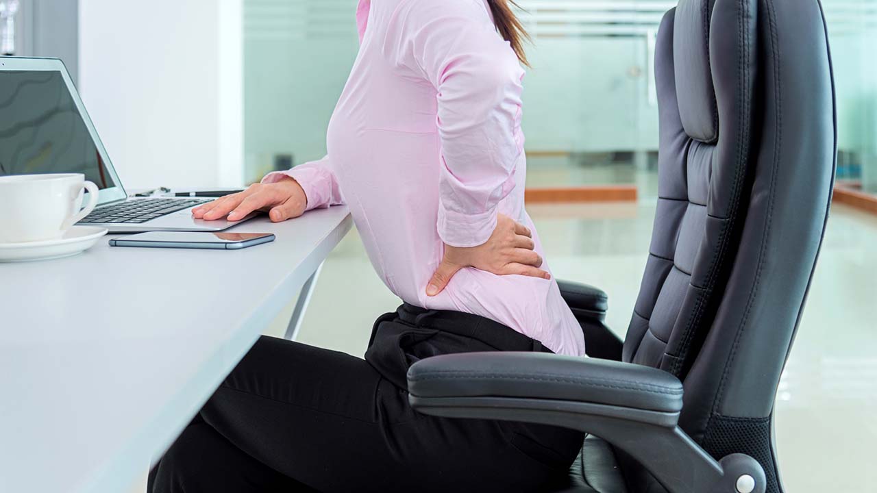 woman sitting at a computer desk holding her back in pain