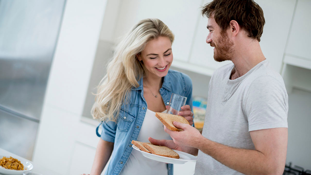 Young couple standing in the kitchen holding a plate with toast