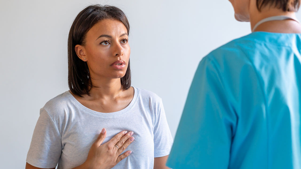 Female patient sitting on exam table pushing on chest while facing nurse