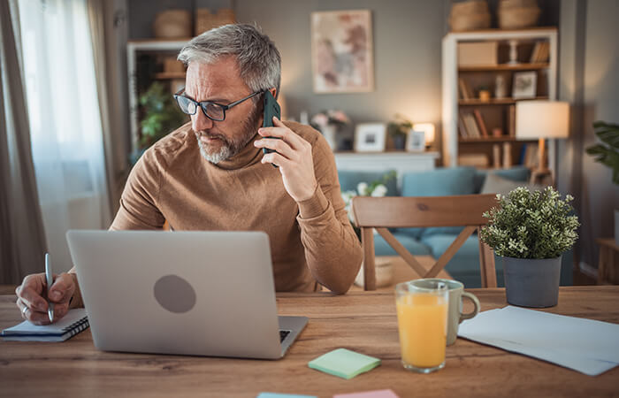 middle aged man speaking on phone while also using laptop and going over insurance