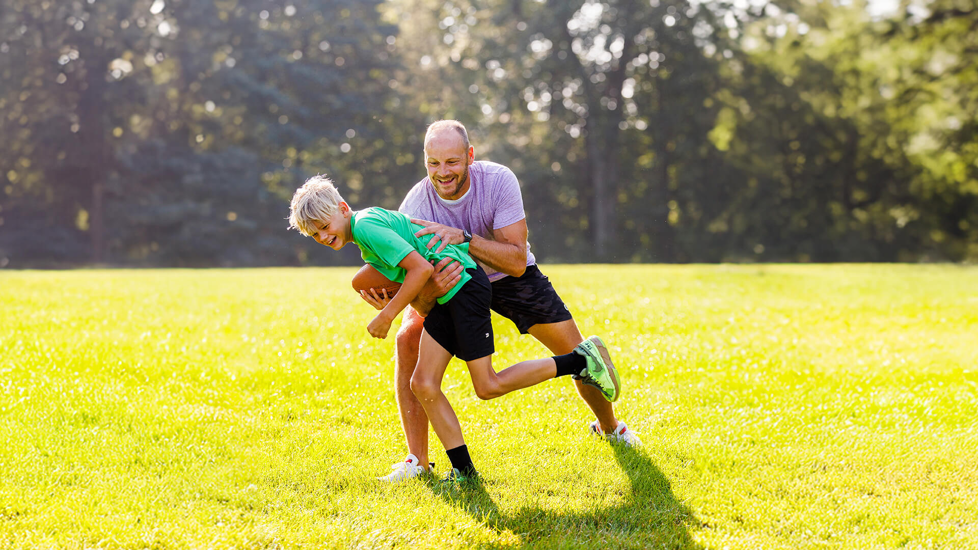 adult man plays football with son outdoors in the backyard