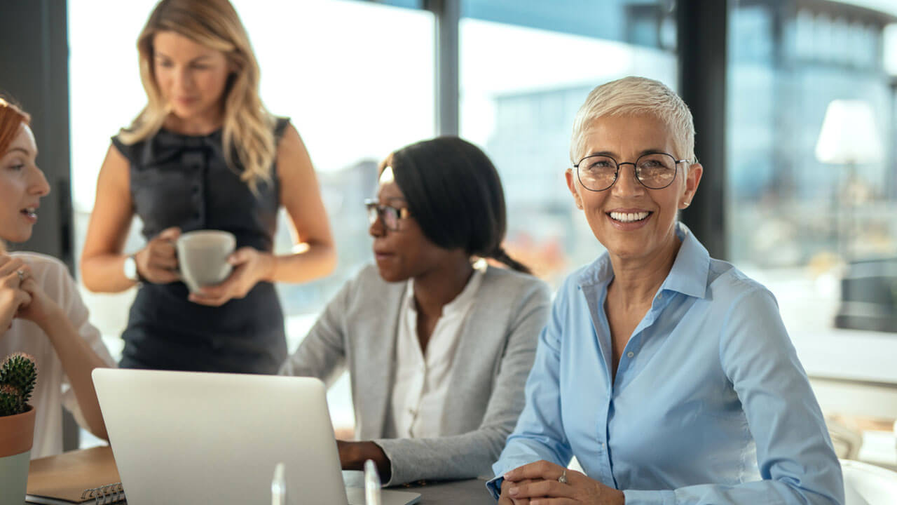 Middle age woman sitting at a table smiling at the camera during a meeting in the workplace