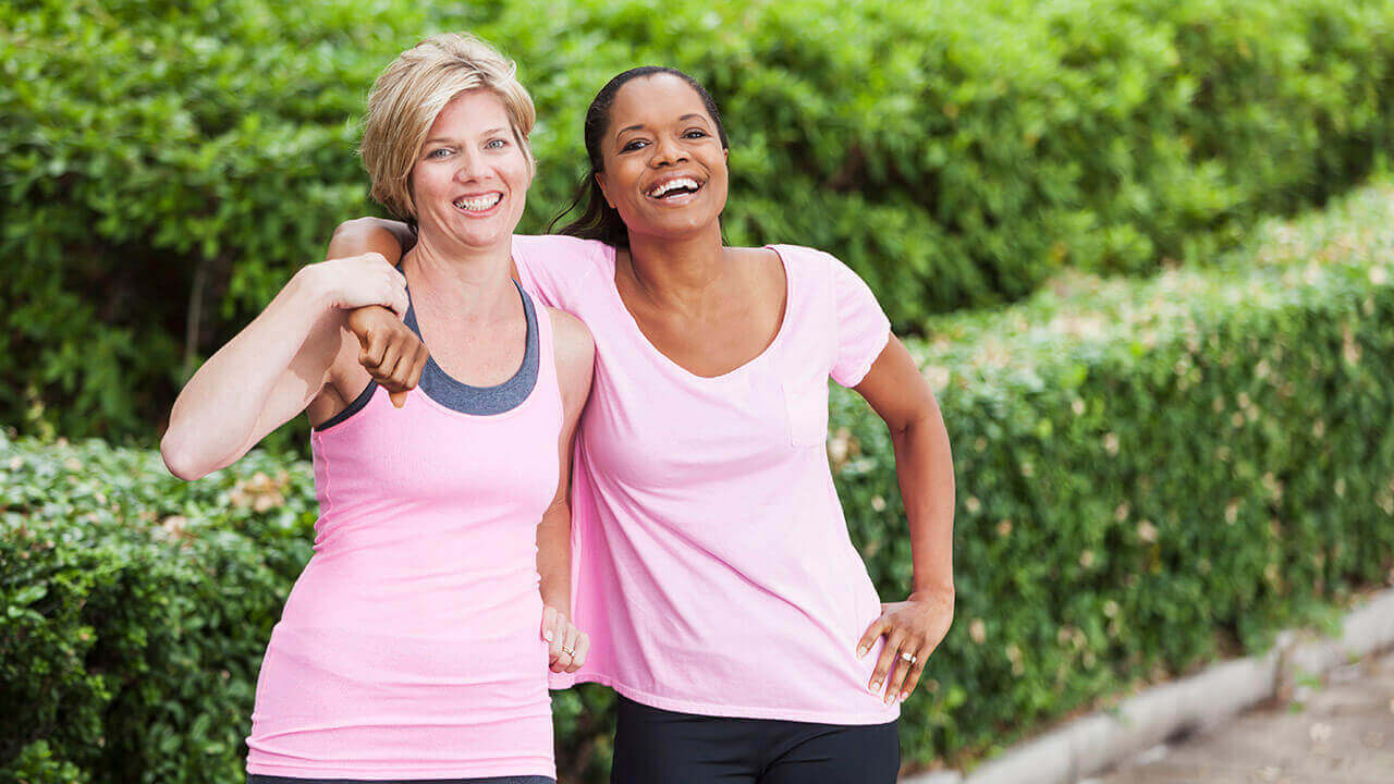 Two women wearing pink shirts leaning on each other outside