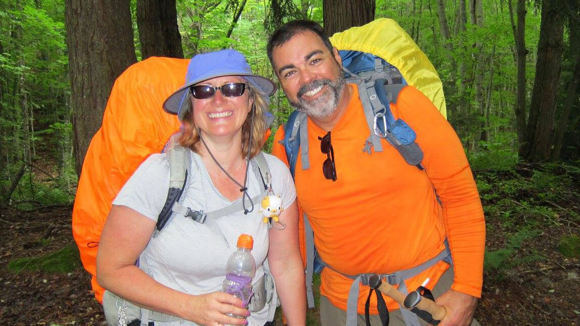 Shannon and Keith smiling wearing backpacks in the woods