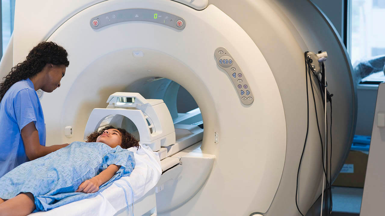 Black female nurse talking to young patient on gurney of MRI machine