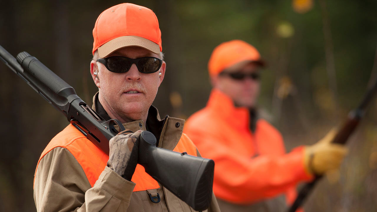 Two men dressed in hunting gear carrying rifles