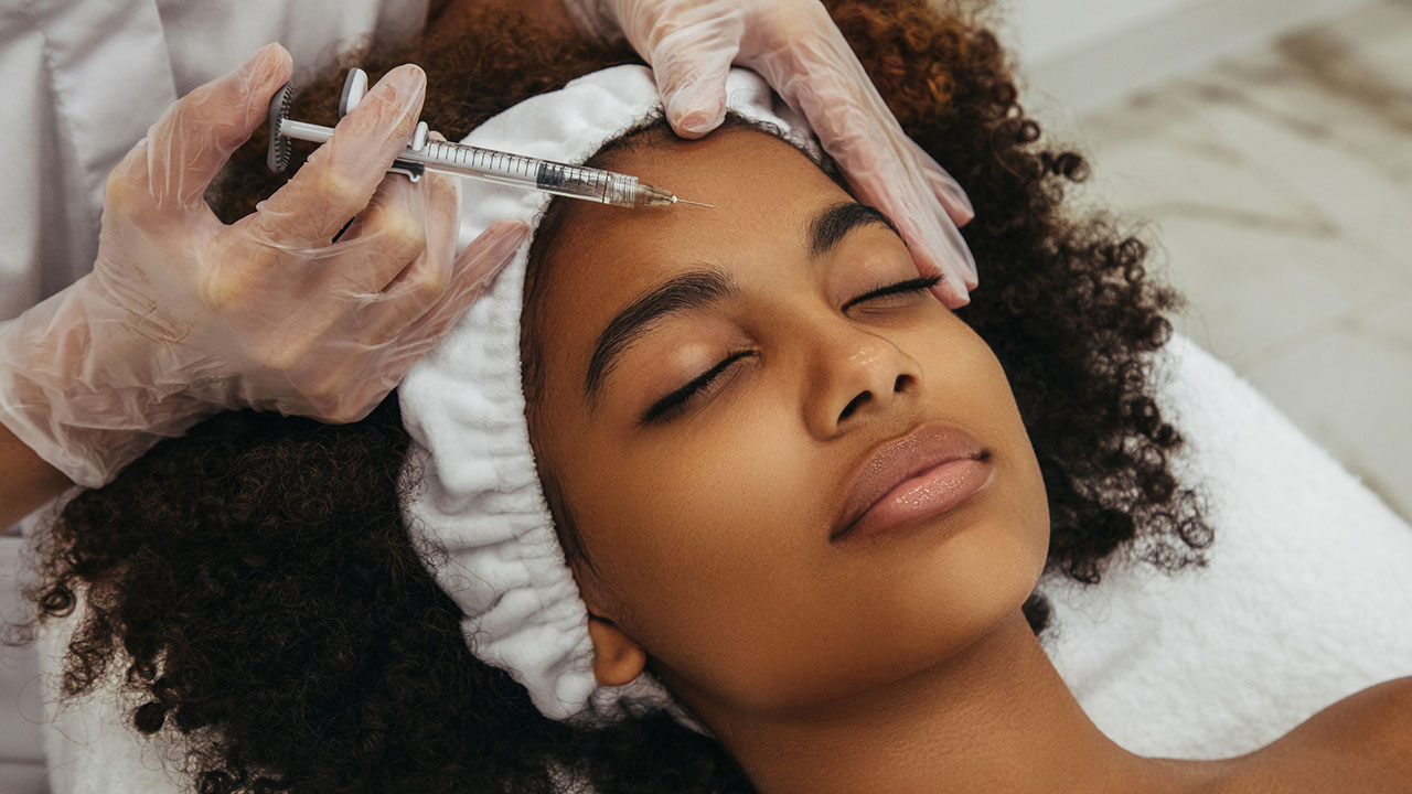 close up of young black women laying on table with a needle over her forhead