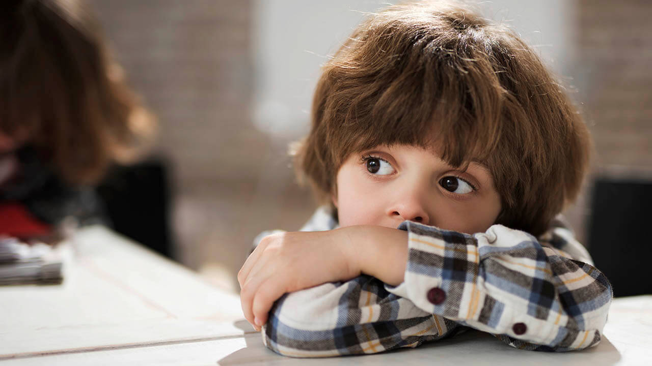 Child with arms crossed on table looking sad
