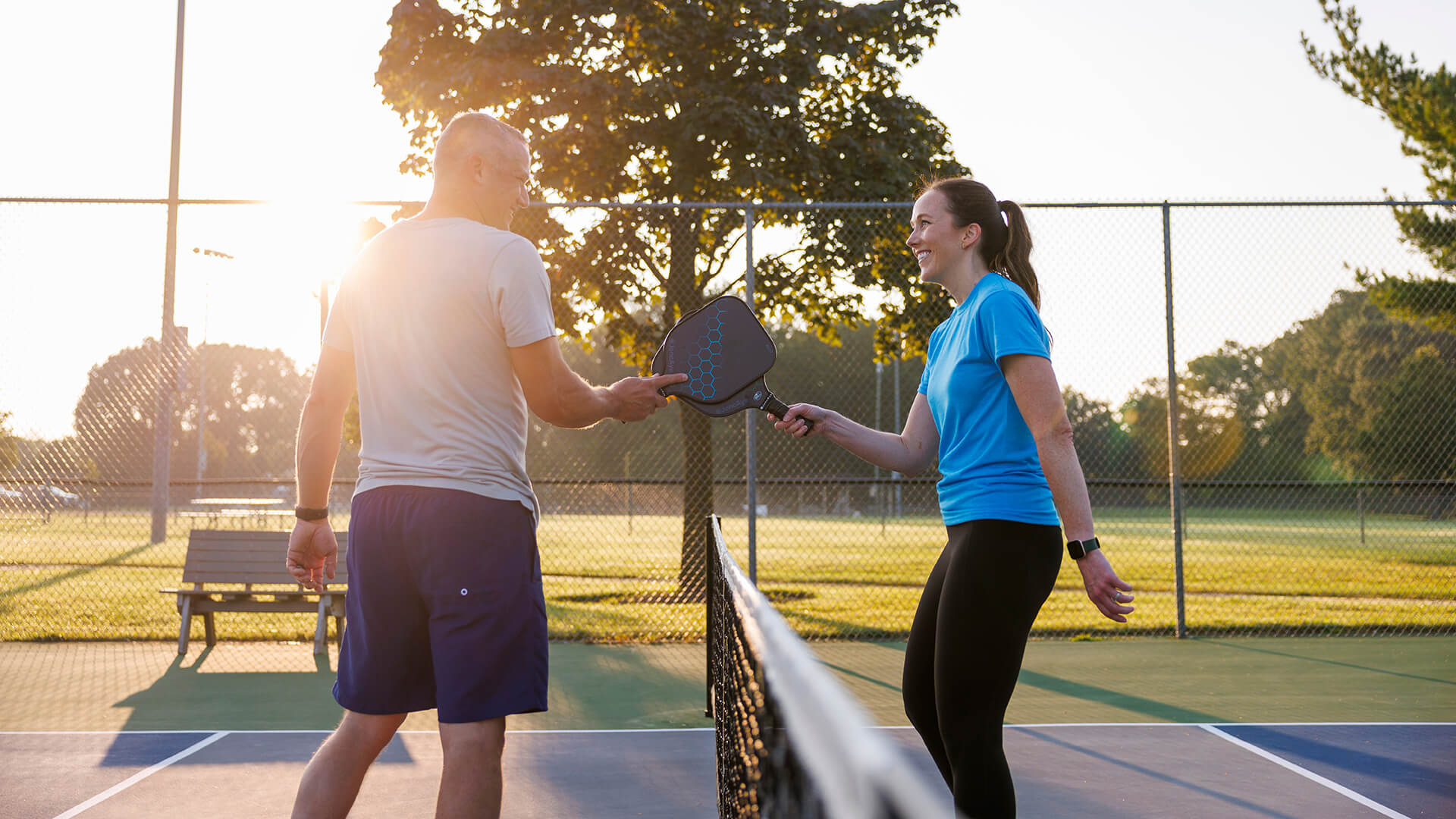 young brunette woman in a blue t-shirt meets middle aged man in gray shirt at pickleball net