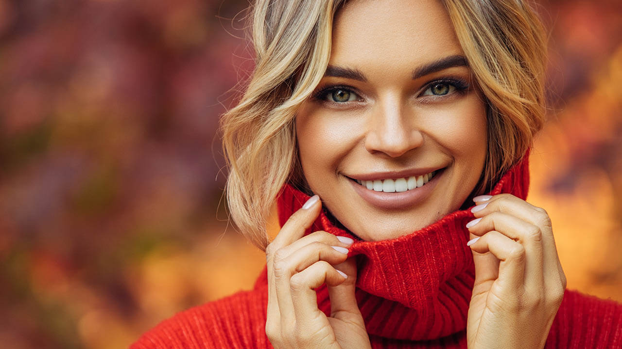 Young woman wearing a red sweater outside with colorful fall leaves behind her