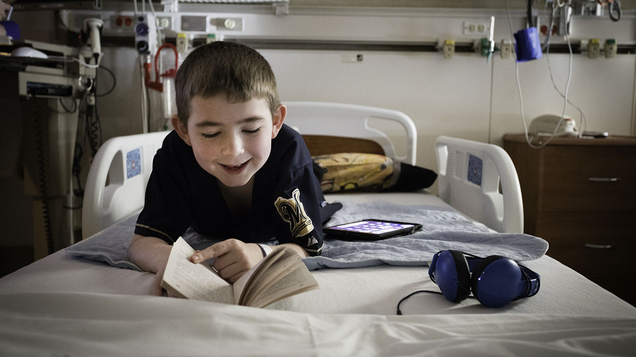 Patient Quentin laying on a hospital bed reading a book and smiling